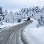 Lone,Truck,Driving,Along,Snowy,Forest,Road,Surrounded,By,Snow-laden